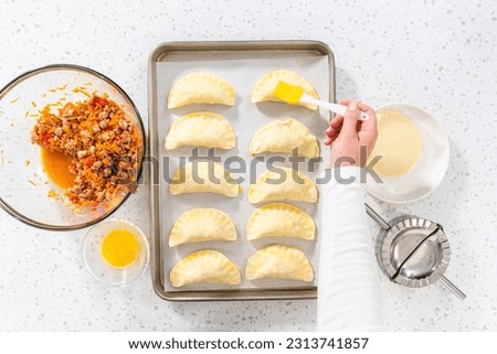 Flat lay. Brushing uncooked turkey empanadas with egg wash.