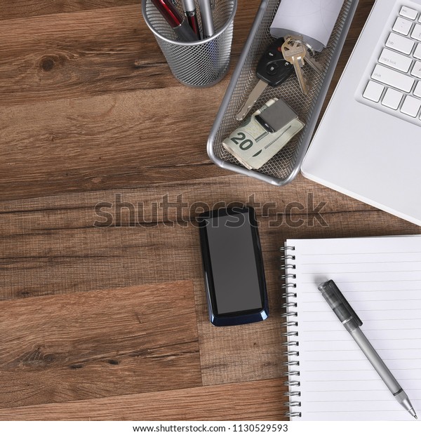 Flat Lay business desk with laptop computer, cell\
phone, money clip, note pad, paper, pen, pen holder car keys with\
copy space.