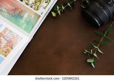 Flat lay. Camera lens, eucalyptus,  photobook, travel memories, dark background brown wood.