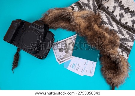 Flat Lay Of Camera, Winter Trapper Hat, US Money, And Travel Documents Isolated On Blue Background