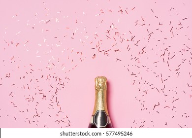 Platt läggning av firande. Champagneflaska med färgglada partystreamers på rosa bakgrund. Stockfoto