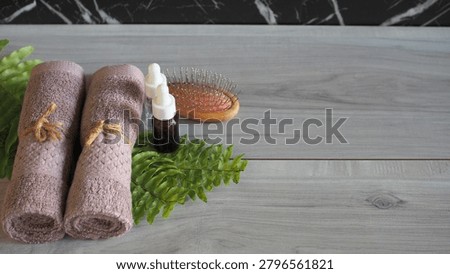 Flat lay close-up of premium spa elements showing white bath salt scattered on a green fern leaf, alongside a mauve pink rolled towel on a light gray wooden background with large copy space.