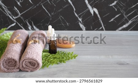 Flat lay close-up of premium spa elements showing white bath salt scattered on a green fern leaf, alongside a mauve pink rolled towel on a light gray wooden background with large copy space.