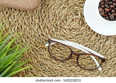 Flat Lay Of Coffee Beans In White Cup, Glasses, Brown Box And Green Grass Placed On Basketery With Copy Space