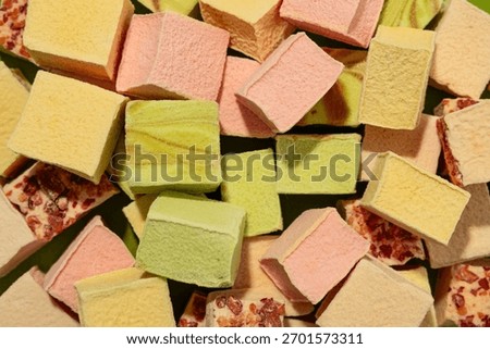 Flat lay of colorful assorted square marshmallows. Pastel sweets in pink, yellow, green, and beige shades, some topped with nuts.