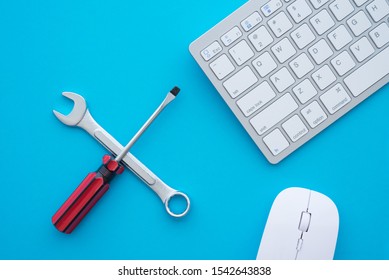 Flat lay of combination spanner or wrench, screwdriver, keyboard computer and mouse on blue background with copy space. Online support, customer care, after sales service and maintenance concept.