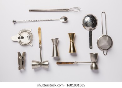 Flat lay composition with bartender iron tools, such as cocktail shaker, jigger, mixing glass, stirring spoon. Background is white.