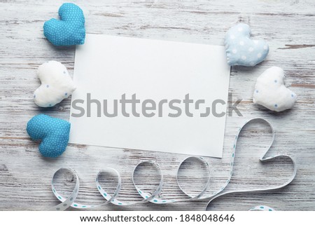 Flat lay composition with blue and white love hearts. Blank sheet of white paper on vintage wooden table. Declaration of love letter. Saint Valentine's day congratulation. Romantic event invitation.