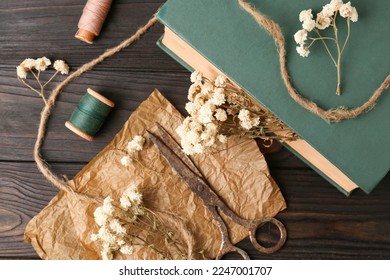 Flat lay composition of book with flowers as bookmark and scissors on wooden table