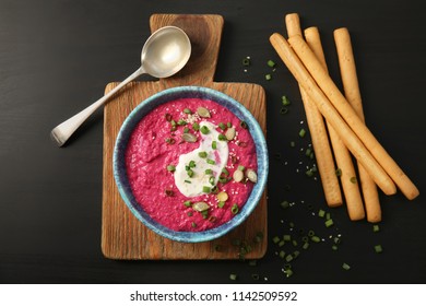 Flat lay composition with bowl of tasty beet hummus and bread sticks on dark background