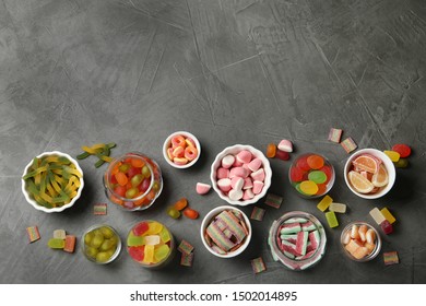 Flat lay composition with bowls of different jelly candies on black stone background. Space for text