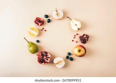 Flat lay composition with circle made of fresh fruits including apple, pear, pomegranate, lemon and grapes on pastel beige background with copy space. Top view