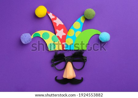 Flat lay composition with clown's face made of party glasses and hat on purple background