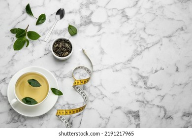 Flat lay composition with cup of diet herbal tea and measuring tape on white marble background, space for text
