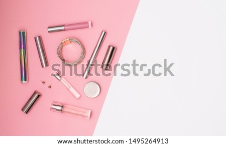 Flat lay composition with decorative makeup products and gold chain necklace on pastel pink background. Makeup and beaty concept. Copy space.