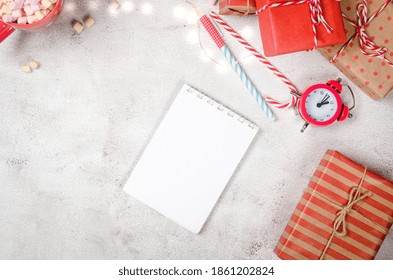 Flat lay composition with diary book for writing down New Year's plans with red Christmas  decorations, cup of cocoa with marshmallows, alarm and gifts. Planing New Year. Goals in notebook 