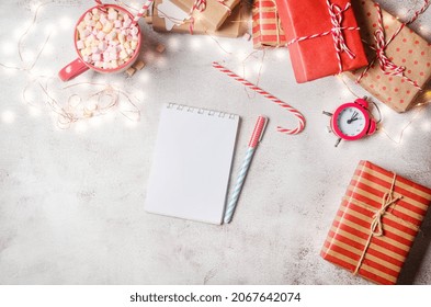 Flat lay composition with diary book for writing down New Year's plans with red Christmas  decorations, cup of cocoa with marshmallows, alarm and gifts. Planing New Year. Goals in notebook 