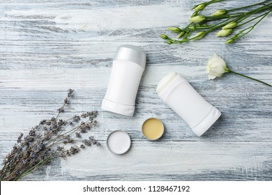 Flat lay composition with different deodorants and flowers on wooden background
