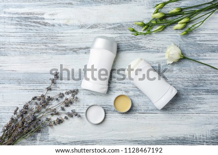 Flat lay composition with different deodorants and flowers on wooden background