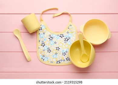 Flat Lay Composition With Drool Baby Bib And Plastic Dishware On Pink Wooden Background