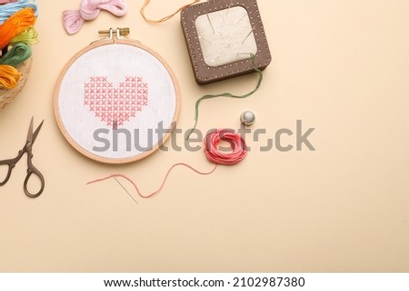 Flat lay composition with embroidery and different sewing accessories on beige background. Space for text