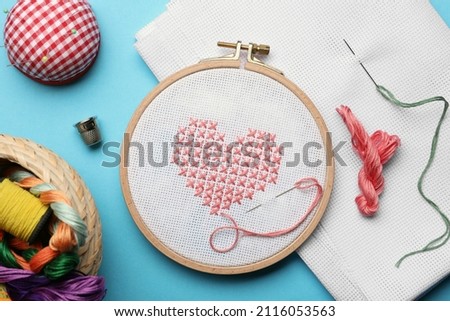 Flat lay composition with embroidery and different sewing accessories on light blue background
