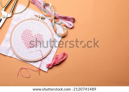 Flat lay composition with embroidery and different sewing accessories on orange background. Space for text