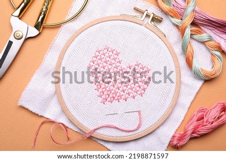 Flat lay composition with embroidery and different sewing accessories on orange background