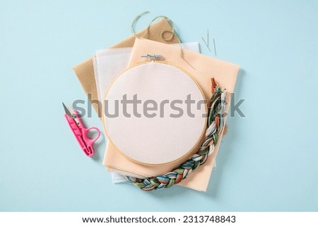 Flat lay composition with embroidery hoop and sewing accessories on blue background. Cross stitch concept.