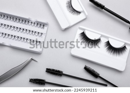Flat lay composition with fake eyelashes, brushes and tweezers on light grey background