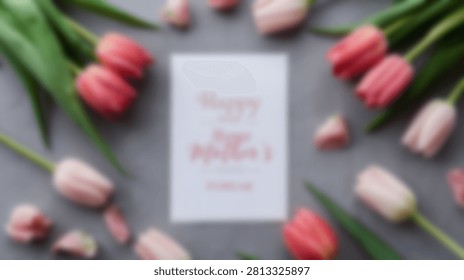 A flat lay composition featuring a bouquet of pink and red tulips surrounding a white card with handwritten text on a textured grey surface.