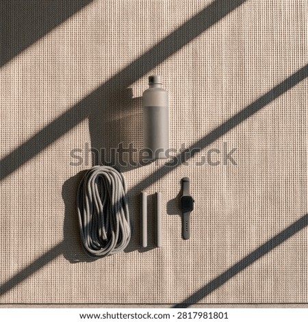 A flat lay composition featuring crafting tools including a spool of rope, a bottle, and other small items, set against a textured background with strong diagonal light and shadow patterns.