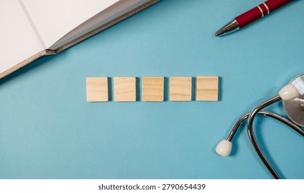 A flat lay composition featuring five wooden blocks arranged in a row on a blue background. Nearby, a red pen and a stethoscope are visible, suggesting a theme of health or education. The lighting is 