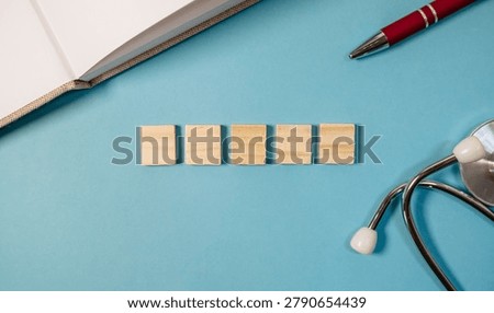 A flat lay composition featuring five wooden blocks arranged in a row on a blue background. Nearby, a red pen and a stethoscope are visible, suggesting a theme of health or education. The lighting is 