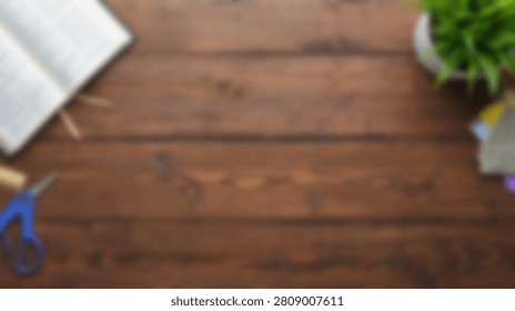 A flat lay composition featuring an open book, scissors, a small potted plant, and other stationery items on a rustic wooden desk surface.