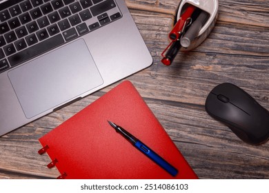 A flat lay composition featuring a red notebook, fountain pen, laptop, and mouse on a rustic wooden desk, representing modern workspace essentials for productivity and organization.