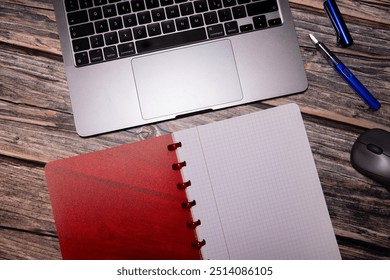 A flat lay composition featuring a red notebook, fountain pen, laptop, and mouse on a rustic wooden desk, representing modern workspace essentials for productivity and organization.