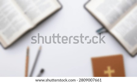 A flat lay composition featuring two open Bibles and a small brown holy book with a golden cross symbol, alongside writing utensils on a clean white surface.