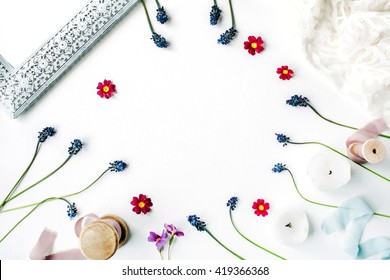 flat lay composition with flowers and decor: muscari, photo frame, white dress, spool with beige and blue ribbon.