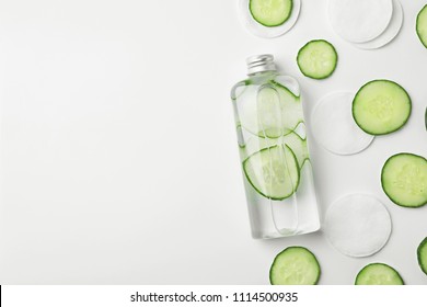 Flat lay composition with fresh cucumber skin care tonic and cotton pads on white background