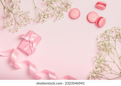 Flat lay composition with gift box, macaroons, satin ribbon and gypsophila on pink background. Stylish invitation. Postcard