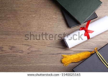 Flat lay composition with graduation hat and student's diploma on wooden table, space for text