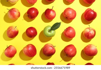 Flat lay composition with green apple surrounded by red ones on yellow background