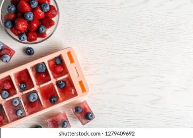Flat lay composition with ice cube tray and berries on wooden background. Space for text