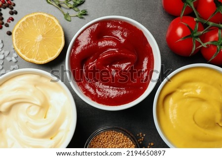 Flat lay composition with ketchup, mustard, mayonnaise and ingredients on grey table
