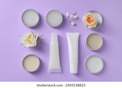 Flat lay composition with lip balms and flowers on lilac background