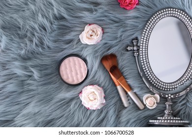 Flat lay composition with makeup brushes, roses and mirror on faux fur