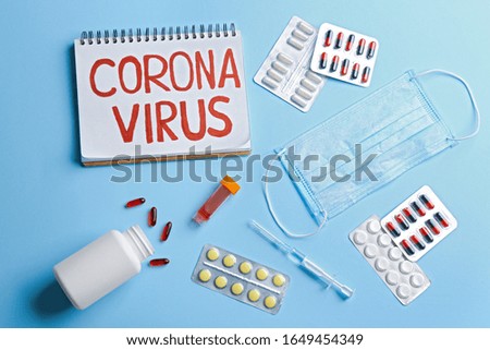 Flat lay composition of medications and notebook with words CORONA VIRUS on light blue background