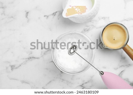 Flat lay composition with mini mixer (milk frother), whipped milk in glass and coffee at white marble table. Space for text