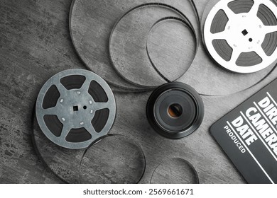 Flat lay composition with movie clapper, film reels and camera lens on grey textured table